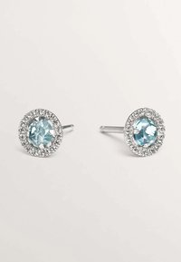 Pendientes de plata con stud que presentan piedras redondas de color azul claro rodeadas por una banda circular de cristales transparentes. Superficie suave y acabado pulido.