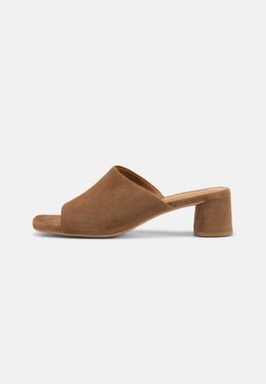 Καφέ σουέντ mule σανδάλι με ανοιχτό δάχτυλο, φαρδιά λουρί και χαμηλό τετράγωνο τακούνι σε απλό ανοιχτό φόντο.