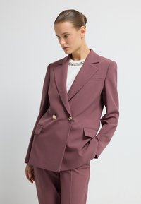 Gestructureerde, dubbele blazer in mauve met gouden knopen, met revers en zijzakken, gecombineerd met een witte top met versieringen.