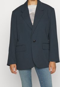 Ciemnoniebieski, oversize marynarka z pojedynczym czarnym guzikiem, klapami, dwoma przednimi kieszeniami i długimi rękawami. Gładka faktura materiału.