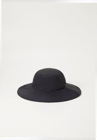 Cappello a secchiello nero realizzato in tessuto leggero e lucido. Caratterizzato da una larga visiera, una parte superiore arrotondata e un sottile motivo strutturato.
