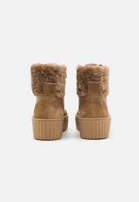 Bottes courtes couleur fauve avec doublure en fausse fourrure au sommet, texture en daim, et semelle en caoutchouc côtelée. Équipées d'une languette à l'arrière pour un enfilage facile.