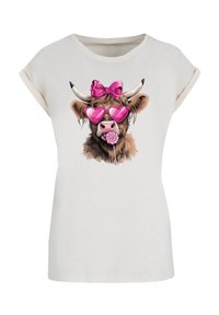 Light-colored t-shirt featuring a graphic of a cow in heart-shaped pink sunglasses, with a pink bow and a lollipop in its mouth.