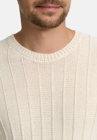 Lys beige strikket genser med ribbestruktur og rund hals. Stoffet er tykt, med vertikale linjer og åpne masker.