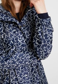 Navy blue waterproof jacket with white star pattern, featuring a hood, zip closure, and elastic cuffs; pockets at the waist.