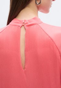 Top rosa a coste con collo alto e apertura a goccia sulla schiena, con tessuto liscio a contrasto sulle spalle.