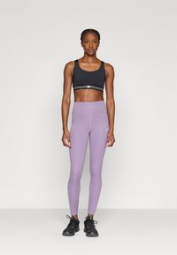 Αθλητικό σουτιέν σε μαύρο με ριγωτή ζώνη, σετ με ψηλόμεσο λεβαντίνι κολάν και μαύρα αθλητικά παπούτσια με πράσινες λεπτομέρειες.