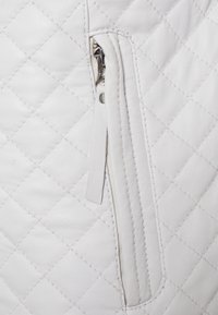 Tissu en cuir blanc matelassé avec une fermeture éclair argentée verticale et une languette en cuir blanc sur le côté droit.