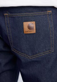 Denim jeans in een donkerblauwe kleur, met een leren logo patch op de achterzak, contrasterende gele stiksels en een klassieke pasvorm.