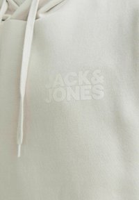 Light gray hoodie made of soft fabric, featuring a kangaroo pocket and a drawstring. The brand logo "JACK & JONES" is embossed on the front.