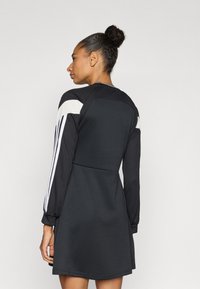 Juoda suknelė su ilgomis rankovėmis, rankovėse baltos juostos, aptempta liemenėle ir platėjanti sijono dalis. Pagaminta iš lygaus, tampraus audinio.