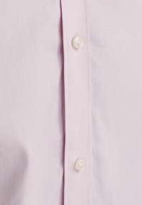 Helles rosa Hemdenmaterial mit strukturierter Oberfläche, das eine Reihe von perlenartigen Knöpfen und sichtbaren Nähten entlang der Knopfleiste aufweist.