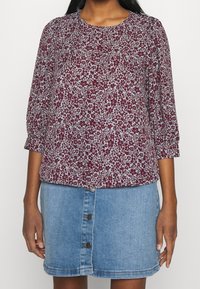 Burgunderfarvet blomsterbluse med trekvartærmer, rund halsudskæring og en lyseblå denimnederdel med knapper ned langs fronten.