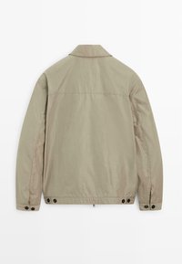 Béžová lehká bunda s dlouhými rukávy, nastavitelné manžety na knoflíky, límec a knoflíkové detaily na spodním lemu v oblasti pasu.