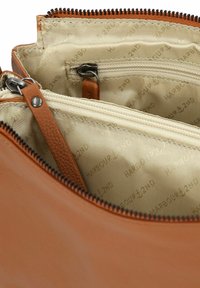 Interno della borsa in pelle color tan con un compartimento con zip e fodera beige stampata con "HARBOUR 2ND," presentando superfici lisce e testurizzate.