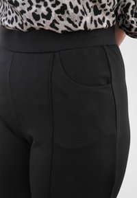 Zwarte, rekbare broeken met een hoge tailleband en een enkele zijzak. Gladde textuur met een klassieke pasvorm, geschikt voor casual wear.