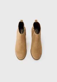 Bottes chelsea en suédine beige avec une texture lisse, dotées d'une fermeture éclair sur le côté et d'une languette à l'arrière pour un enfilage facile. Design à bout rond.