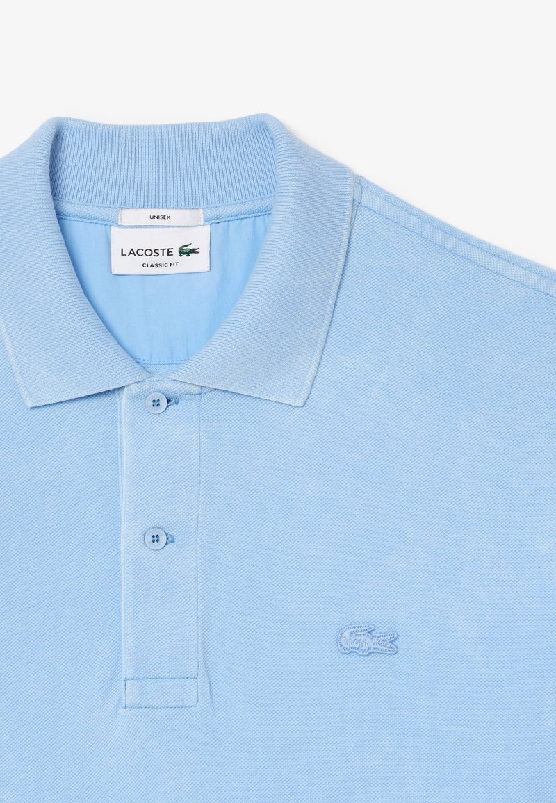 Jasnoniebieska koszulka polo Lacoste, klasyczny krój, z teksturą piké, z kołnierzykiem na stójkę oraz małym, wyszywanym logo na piersi.