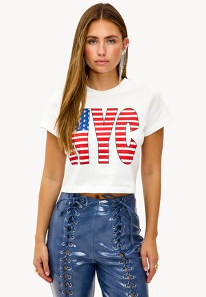 T-shirt blanc court avec un graphisme "NYC" en rouge et bleu, arborant un motif drapeau américain rayé. Associé à un pantalon en simili cuir bleu brillant avec des lacets.