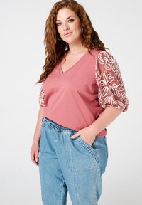Roze V-hals top met witte geborduurde pofmouwen, gecombineerd met lichtblauwe, loszittende jeans met een elastische tailleband en zakken.