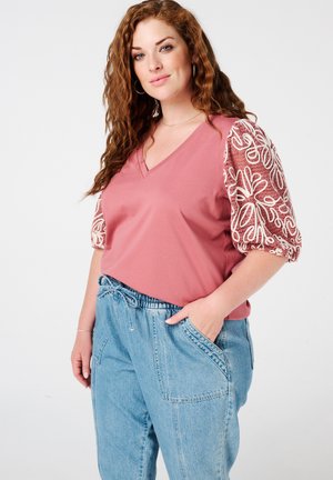 Haut v-neck rose avec des manches puff brodées blanches, associé à un pantalon en denim léger et ample de couleur bleu clair avec une taille élastique et des poches.