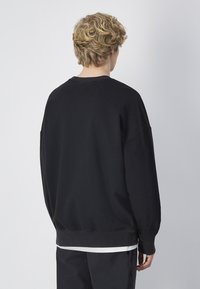 Sudadera negra de corte relajado, con puños y bajo acanalados, y hombros caídos. Tejido suave con una textura lisa, diseño minimalista.