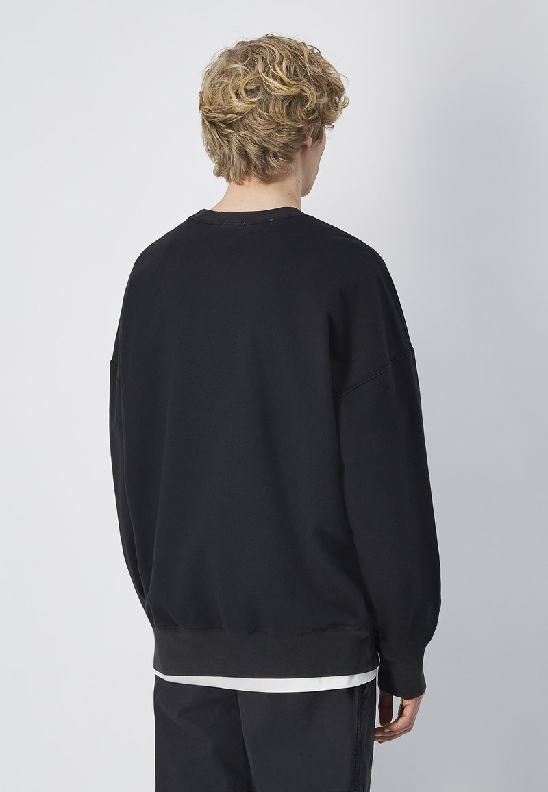 Sweatshirt noir avec une coupe décontractée, des poignets et un ourlet côtelés, et des épaules tombantes. Tissu doux avec une texture lisse, design minimaliste.