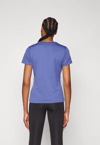 T-shirt roxo de manga curta com decote redondo; tecido suave, design ajustado e detalhes de costura mínimos. Usado com leggings pretas.