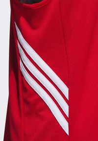Rød atletisk trøje med tekstureret stof, der har tre hvide striber, der løber diagonalt langs siden for kontrast og detalje.