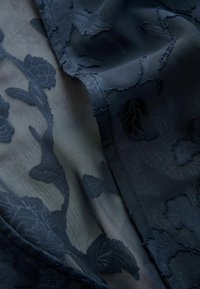 Ciemnoniebieska przezroczysta tkanina z wyrazistymi kwiatowymi wzorami i delikatnymi fałdami, podkreślającymi fakturę i misterny haft.