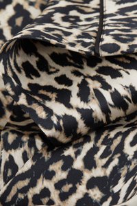 Weicher Stoff mit einem beigen und schwarzen Leopardenmuster, der eine gefaltete Kante mit sichtbaren Nähten zeigt.