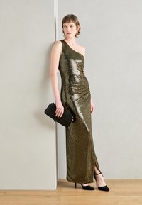 Robe en sequins dorés avec un design à une épaule, des détails froncés et une fente haute. Accompagnée d'une petite pochette noire et de talons noirs.