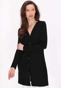 Cardigan nero a maniche lunghe con scollatura a V, bottoni frontali e taglio dritto. Il tessuto appare morbido con una leggera lucentezza e spacchi laterali.