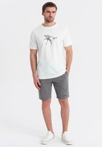 T-shirt en coton blanc avec un graphique de bicyclette et le texte "Profitez du voyage." Associé à un short gris avec des détails de couture et un logo.