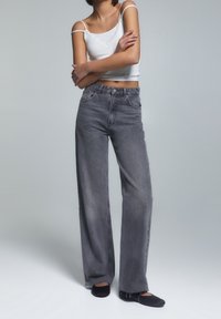 Šedé džíny s vysokým pasem a rovnými nohavicemi se zesvětlenou texturou, kombinované s bílým zkráceným topem a černými balerínami.