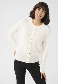 Witte cardigan met lange mouwen, ronde hals en knoopsluiting aan de voorkant; gladde textuur en aangesloten ontwerp met zwarte accenten op de knopen.