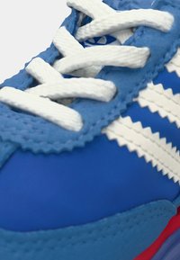 Zilā kedu ar baltām auklām, ar teksturētām akcentiem, zigzaga raksta pārklājumiem un sarkanu zoli.