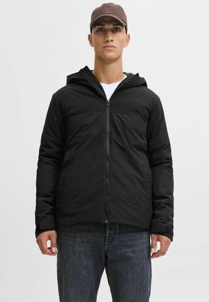 Sort zip-up jakke med hætte og en glat tekstur. Har en vandret søm over brystet og to frontlommer. Komplementeres af denim jeans.
