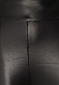 Mustat tekonahka-housut, joissa on sileä pinta ja näkyvät saumat. Paksu vyötärönauha ja hyvin istuva malli.