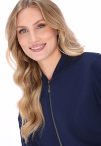 Marineblauw bomberjack met ritssluiting, geribbelde kraag en een gladde textuur. Voorzien van zachte stof en een getailleerde pasvorm.