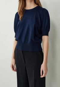 Marinblå stickad tröja med rund halsringning, korta puffärmar och ribbad nederkant. Mjuk textur, något avslappnad passform. Kombinerad med svarta byxor.