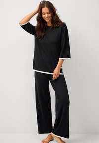Sort loungewear sæt med en løstsiddende top med trekvartærmer og hvide kanter samt brede bukser. Blød og glat tekstur.