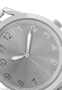 Montre analogique argentée avec un cadran en métal brossé, des chiffres noirs audacieux, des aiguilles des heures et des minutes pointues, et un boîtier en acier inoxydable épuré.