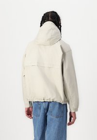 Light beige jacket with a hood, elastic waist, and back pocket detail. Made from a smooth fabric, featuring a slightly oversized fit.