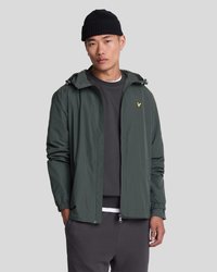 Veste verte légère avec capuche, poignets élastiques et fermeture éclair à l'avant. Présente un petit logo doré sur la poitrine et une texture lisse.