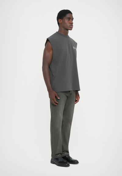 Grijze mouwloze shirt met een losse pasvorm, gecombineerd met olijfgroene rechtlopende jeans en zwarte schoenen. Minimalistisch ontwerp en basiskleuren.