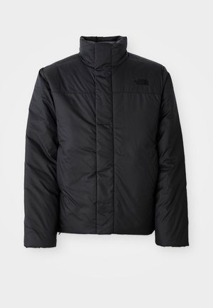 Veste isolante noire avec un col haut, présentant un zip à l'avant et un logo sur la poitrine gauche. Le matériau semble lisse et rembourré.