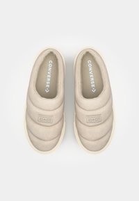 Beige slip-on-sko med quiltet tekstur, med en kremfarget gummisåle og "CONVERSE ALL-STAR" merking på siden.
