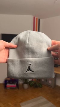 Szürke kötött sapka bordás textúrával és felhajtott passzéval, az elején fekete hímzett Jordan logóval.