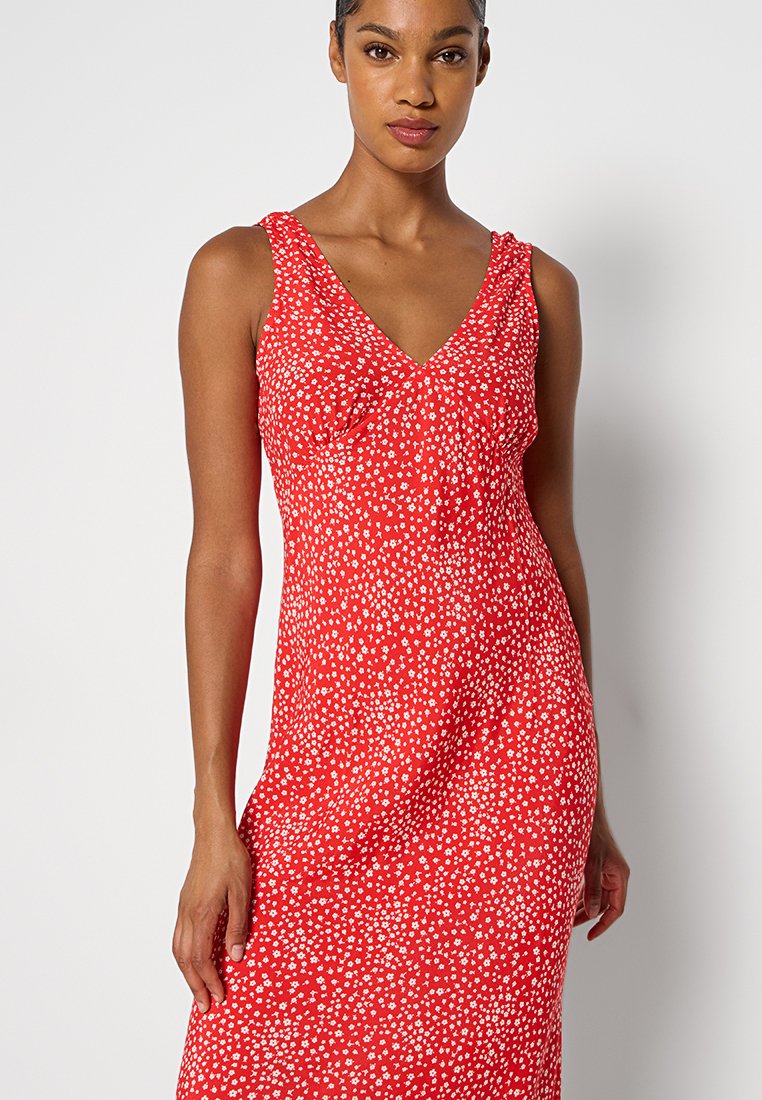 Abito rosso senza maniche con scollo a V, caratterizzato da un motivo floreale bianco. Realizzato in tessuto leggero con una silhouette aderente.